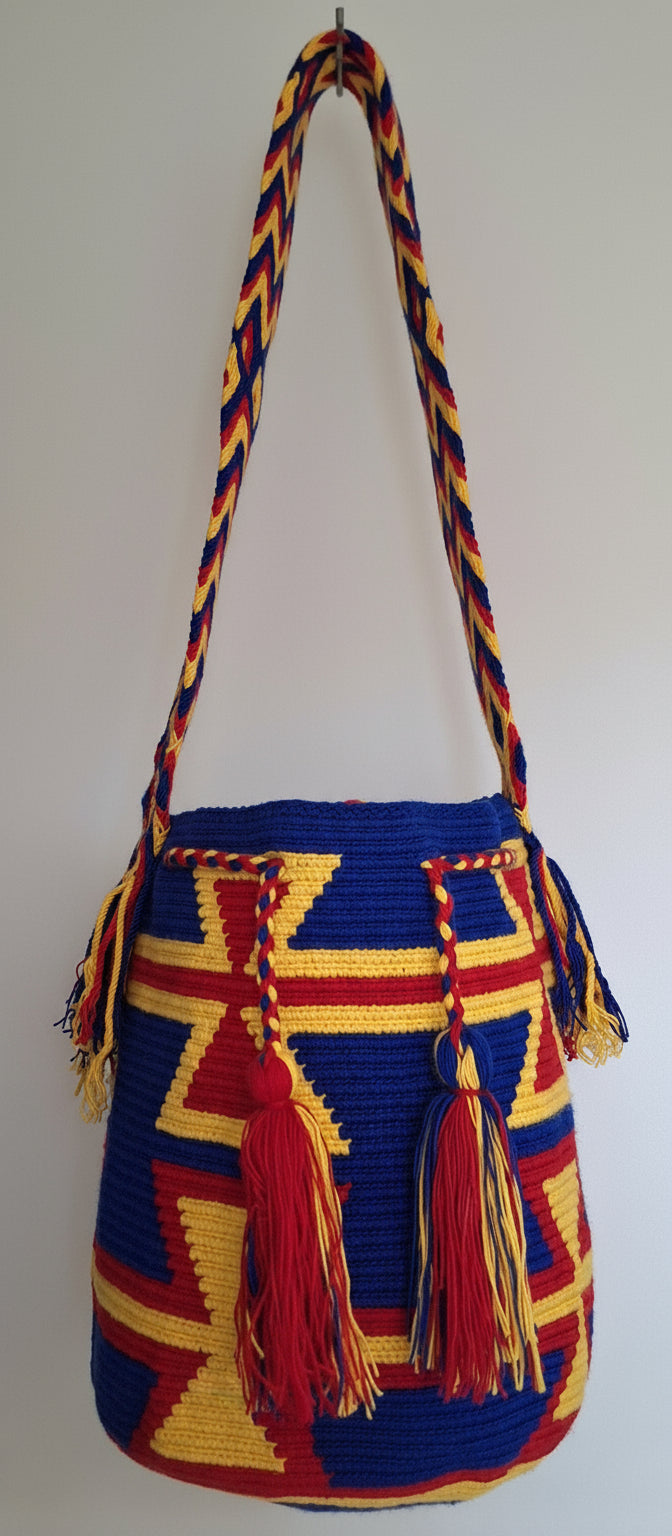 Detailed view of traditional Wayuu crochet technique in red, yellow and blue with tassels on a mochila and crossbody strap fully extended. Large bag is responsibly hand-crafted; a boho festival essential.