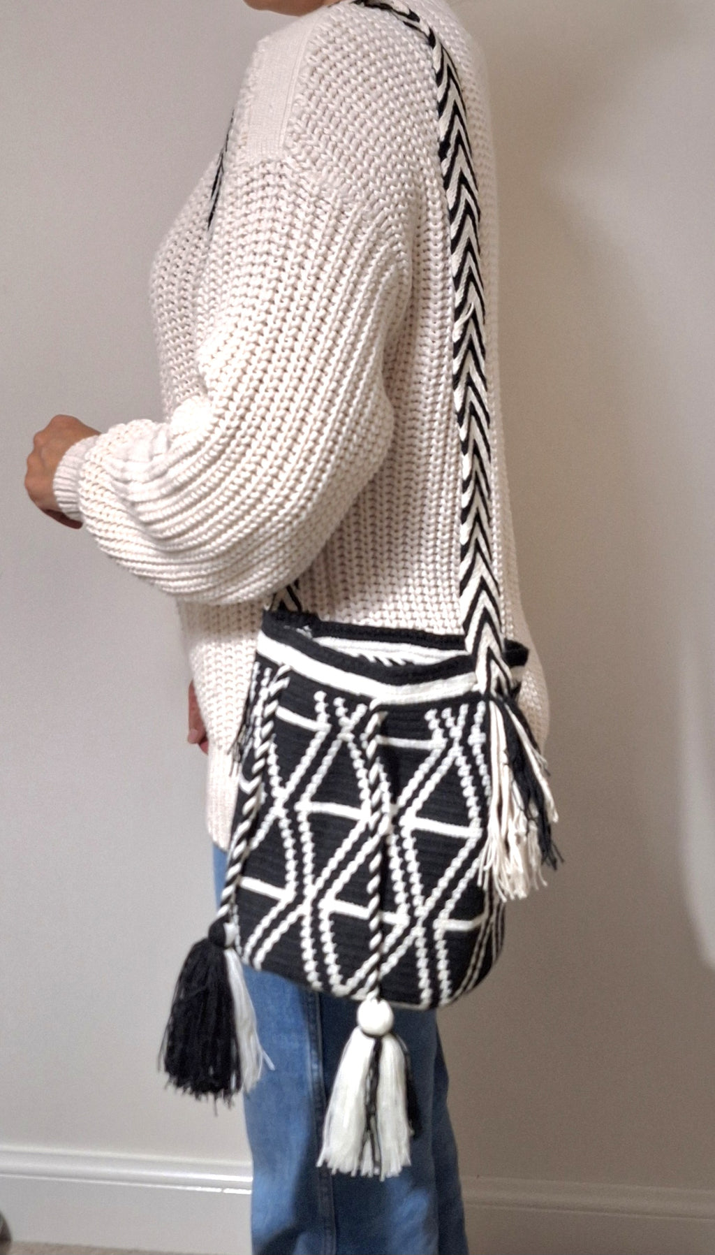Full body shot of woman wearing medium-sized Wayuu bag with triangle design and back and white. Mochila is ethically made, high-quality boho accessory.