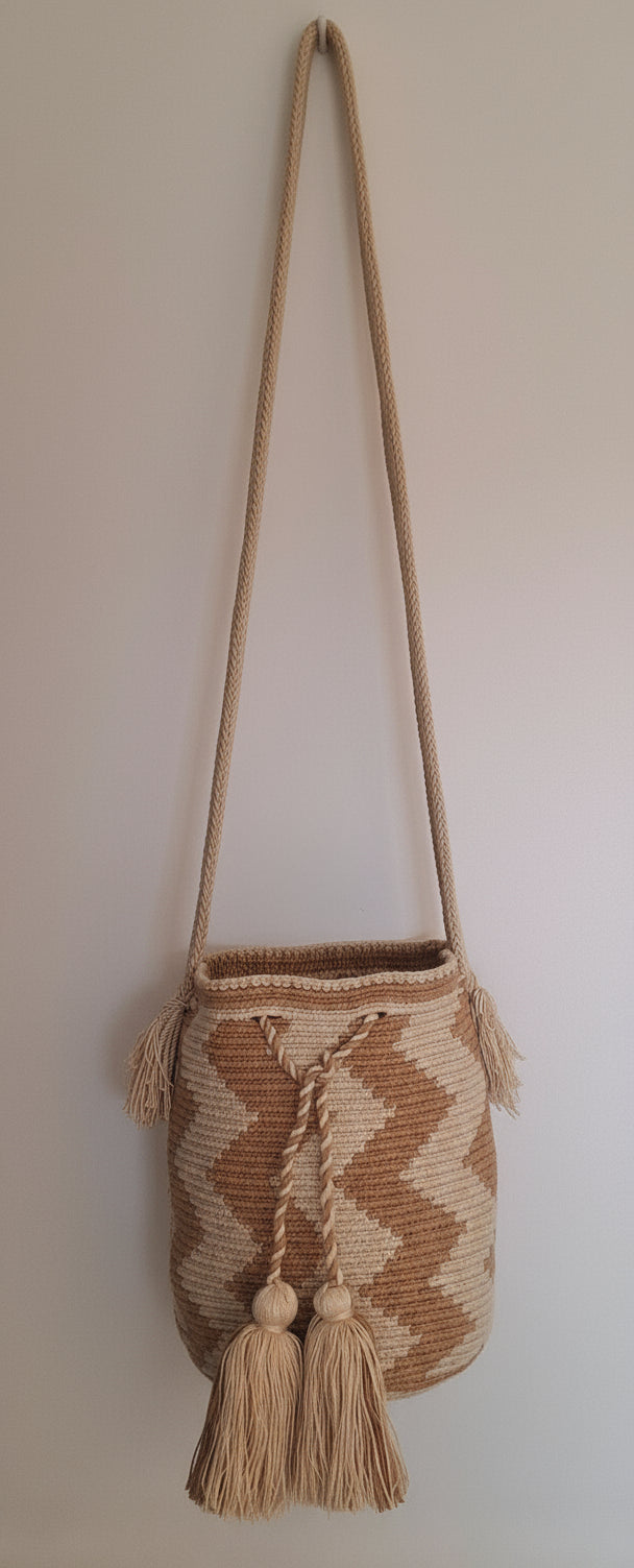 Detailed view of traditional Wayuu crochet technique on cream and beige with zigzag design and tassels on a mochila bag crossbody strap fully extended. Medium-sized bag is responsibly hand-crafted; a boho festival essential.