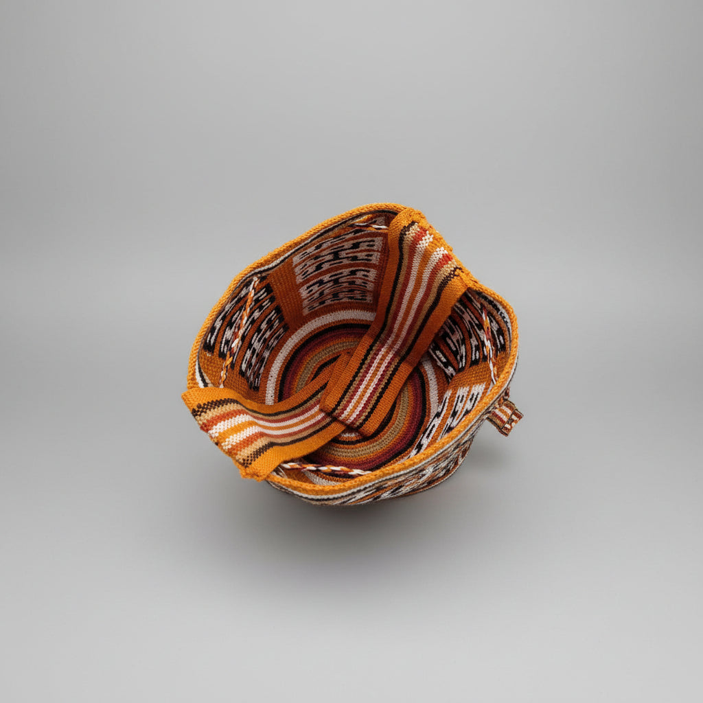 A top-down view of the interior of a handwoven Wayuu mochila, featuring a vibrant ochre, brown, black, and white geometric pattern. 