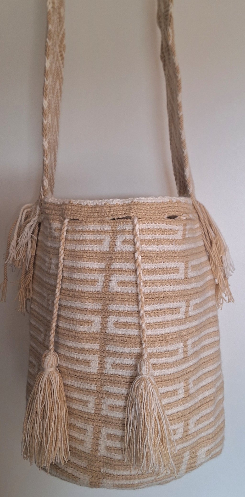 Detailed view of traditional Wayuu crochet technique in cream and white with tassels with crossbody strap fully extended. Mochila bag is traditionally crafted; adds a tribal touch to boho fits.