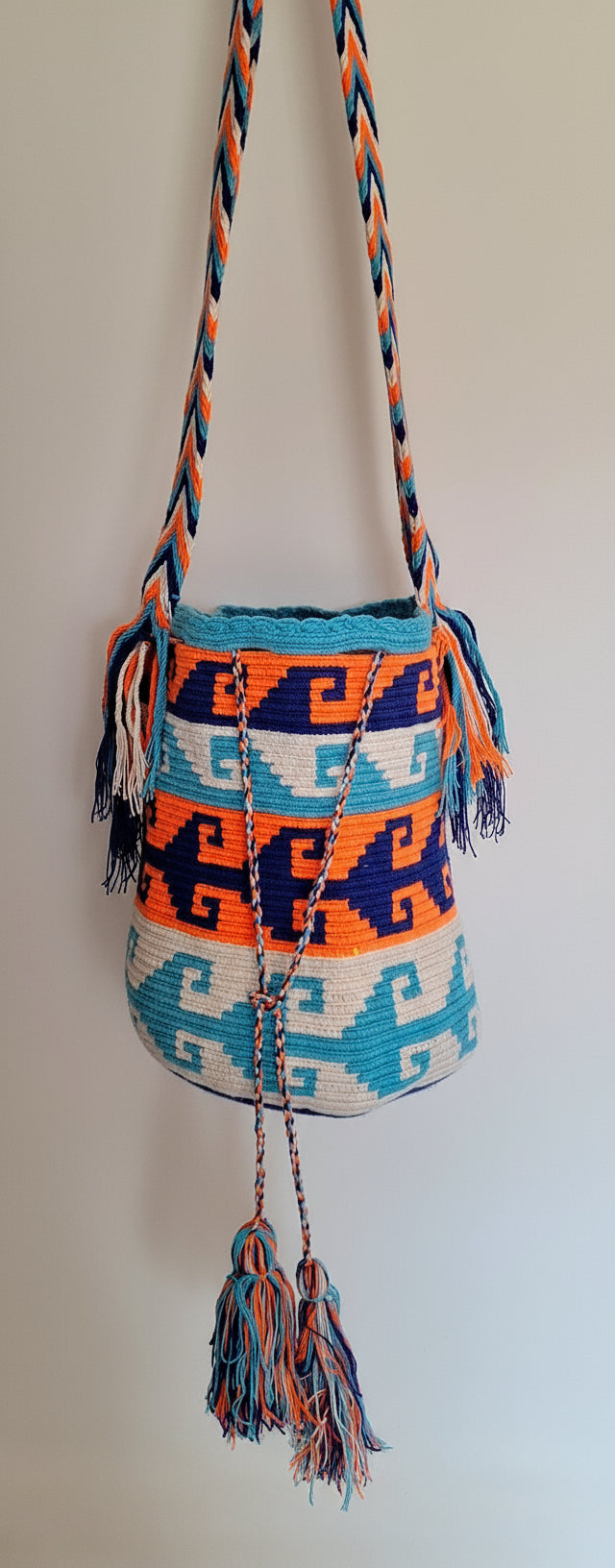 Detailed view of traditional Wayuu Mochila in vibrant marine and orange coloured threads and crashing wave design with crossbody strap fully extended. Bag is fair trade bucket bag for a free-spirited look.