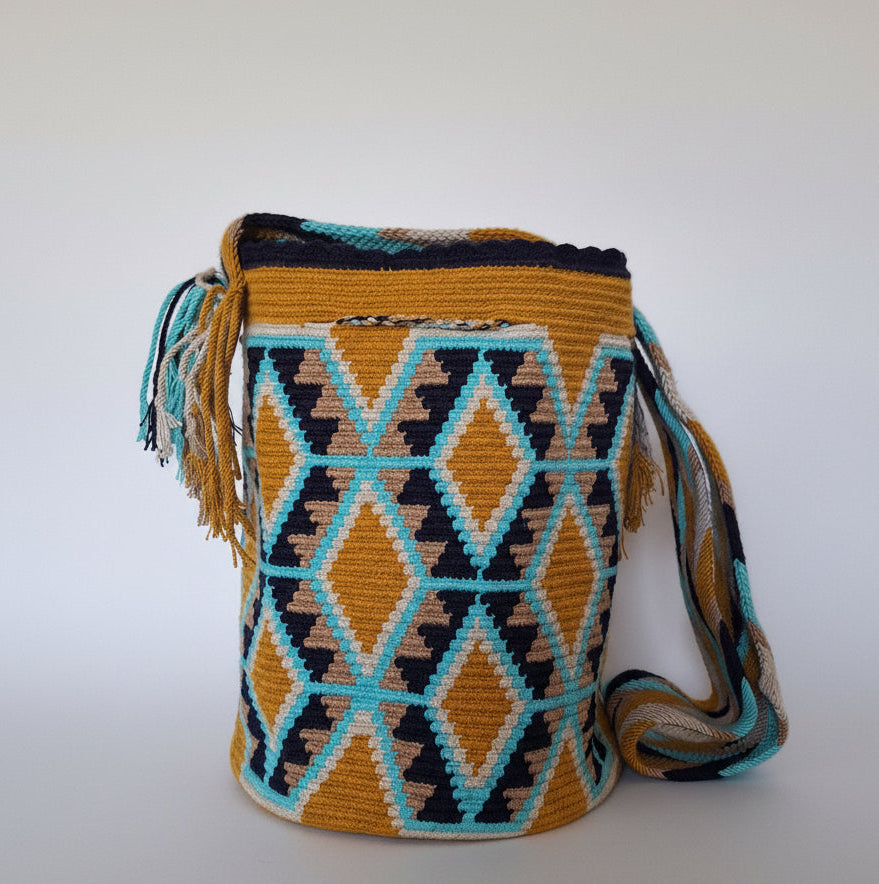 Detailed view of traditional Wayuu crochet technique and tassels on a mochila bag on ochre and blue Ethically and responsibly sourced.