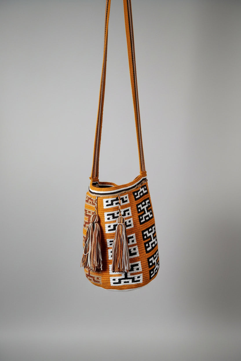 A handwoven bucket bag with a geometric black, white, and vibrant ochre pattern, hanging on studio wall. Focus on the traditional clan design of this ethically-sourced Wayuu mochila.