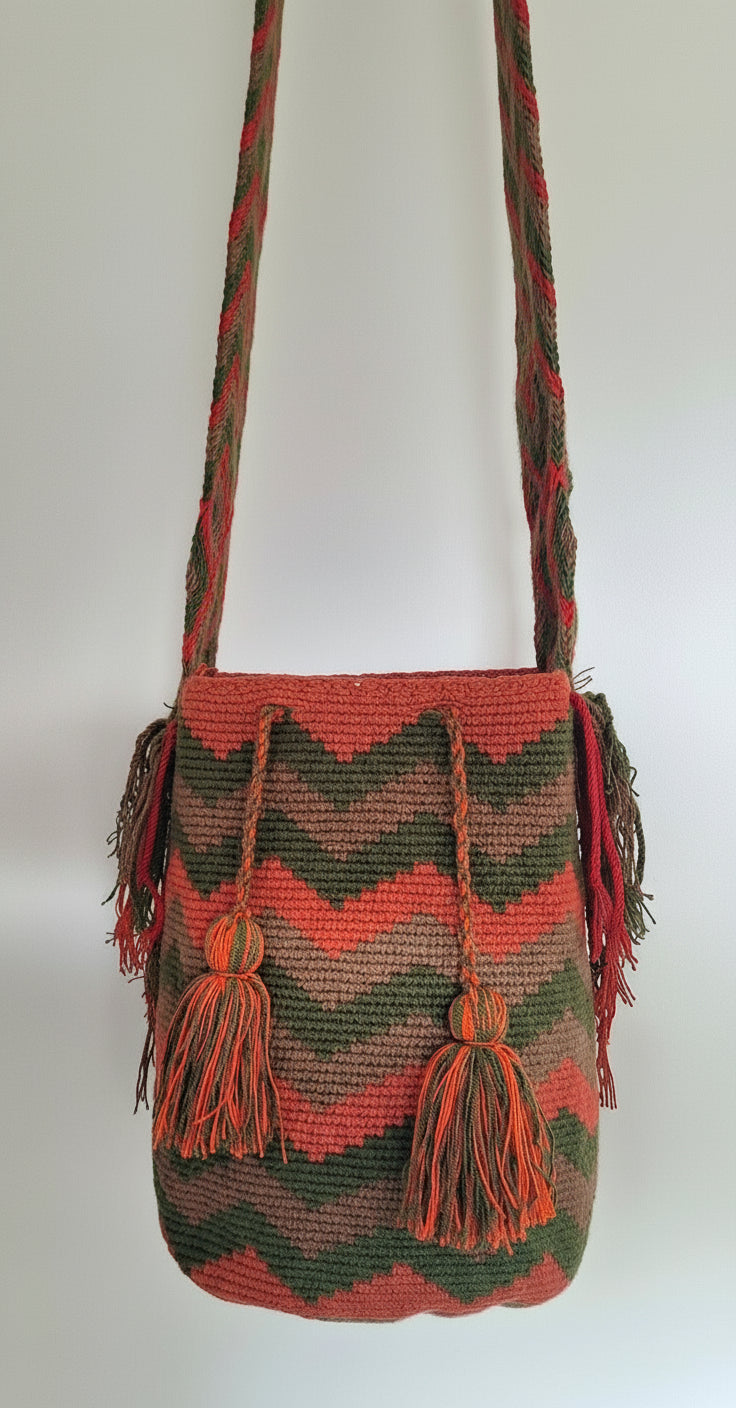 Detailed view of traditional Wayuu crochet technique in red, green and tan  with zigzag design and tassels and crossbody strap fully extended. Large mochila bag is sustainably sourced and styled for boho summer days.