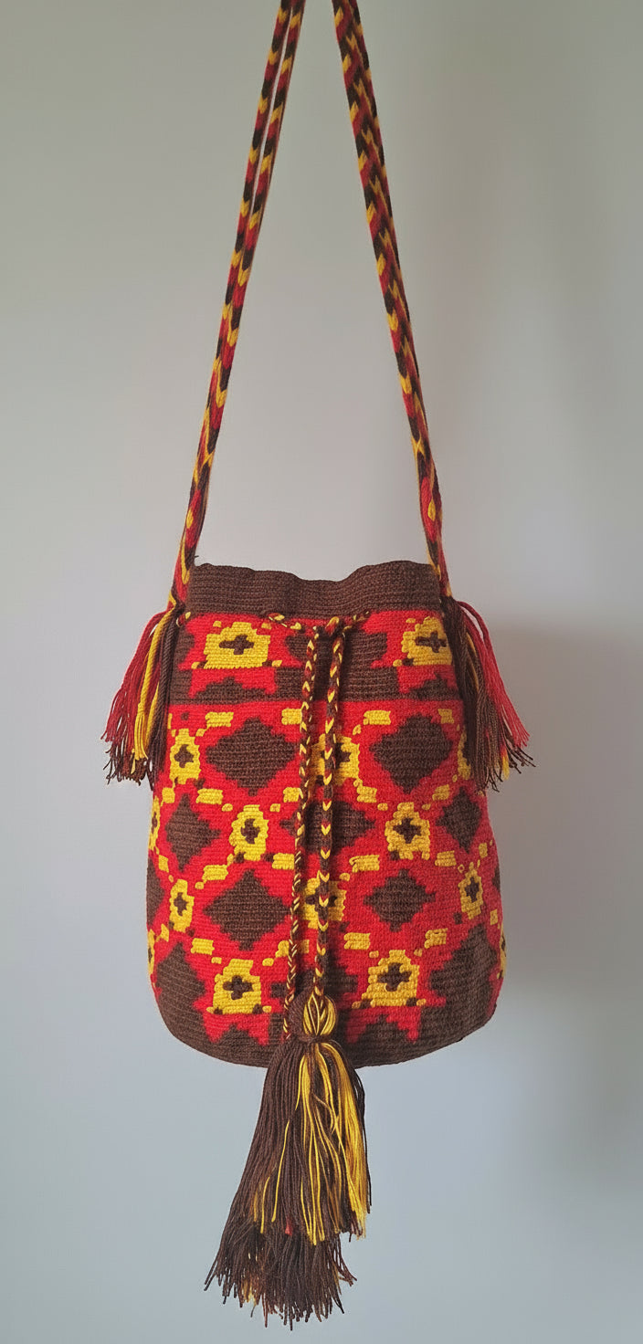Detailed view of traditional Wayuu crochet technique in red, yellow and brown with cross and diamond design and tassels and crossbody strap fully extended. Large mochila bag is authentic Wayuu heritage, ideal for eclectic outfits.