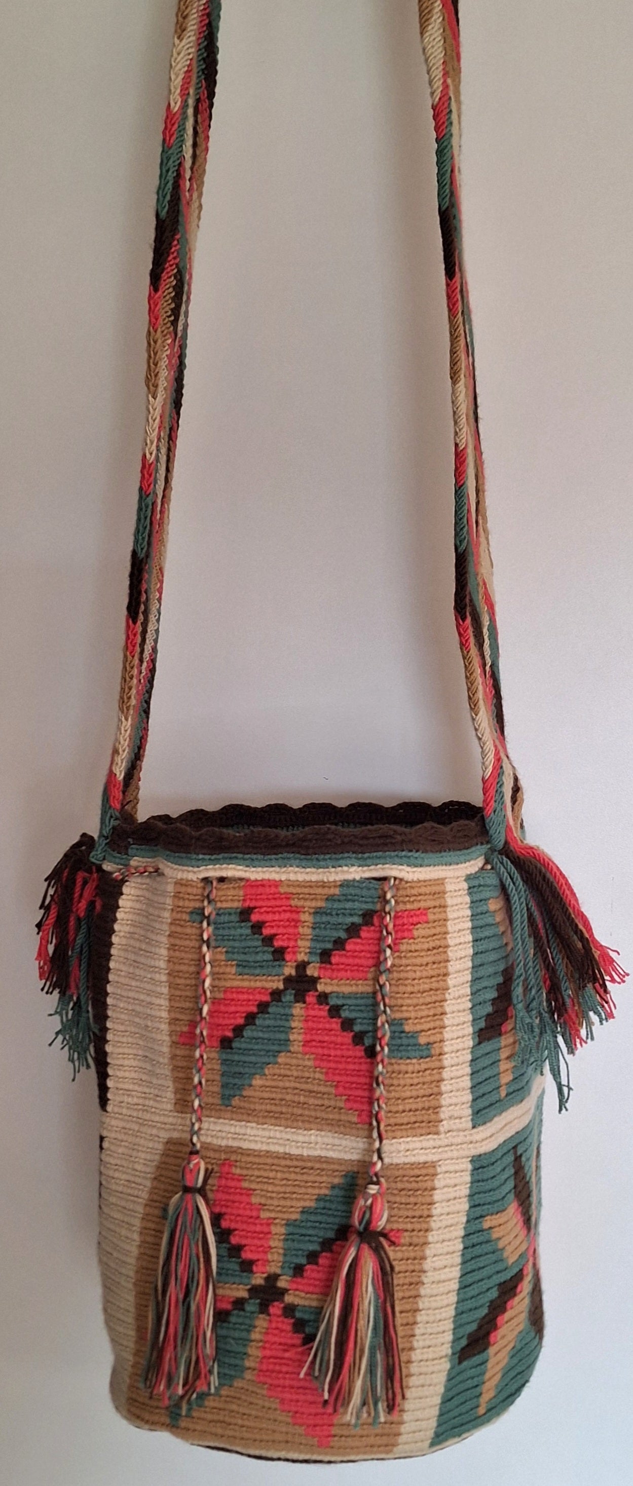 Detailed view of traditional Wayuu crochet technique in pink, turquoise and brown with flower design and tassels on a mochila bag with crossbody strap fully extended. Large bucket bag is responsibly hand-crafted; a boho festival essential.
