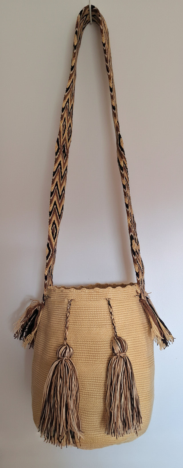 Detailed view of traditional Wayuu bag, light-mustard colour with tassels and crossbody strap fully extended. Wayuu bag is ethically sourced for a conscious boho wardrobe.
