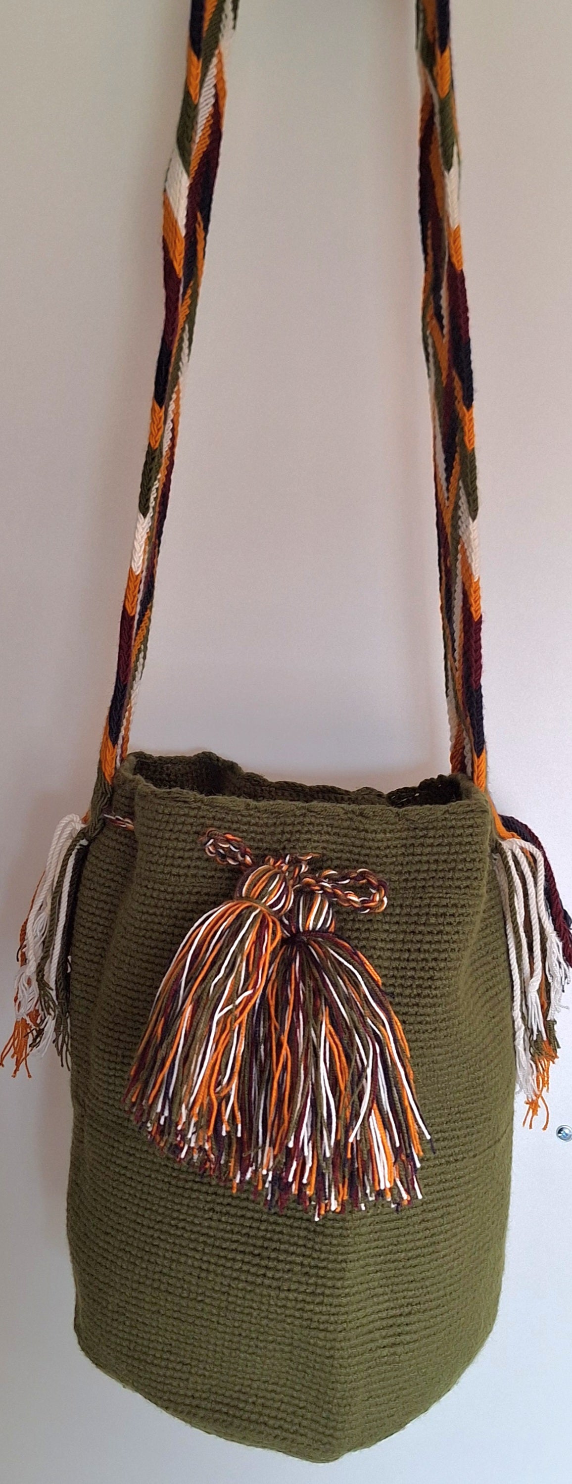 Detailed view of traditional Wayuu crochet technique and tassels on a olive green mochila bag with crossbody strap fully extended. Large mochila is hand-woven by artisans; great for boho-chic layers.