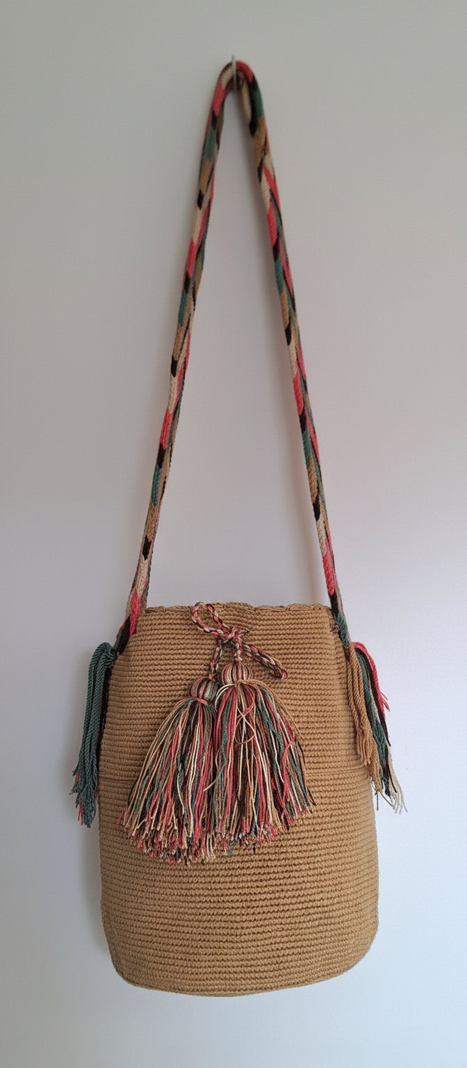 Detailed view of traditional Wayuu crochet technique and tassels on tan-coloured mochila bag with crossbody strap fully extended. Bag is a fair trade bucket bag for a free-spirited look.