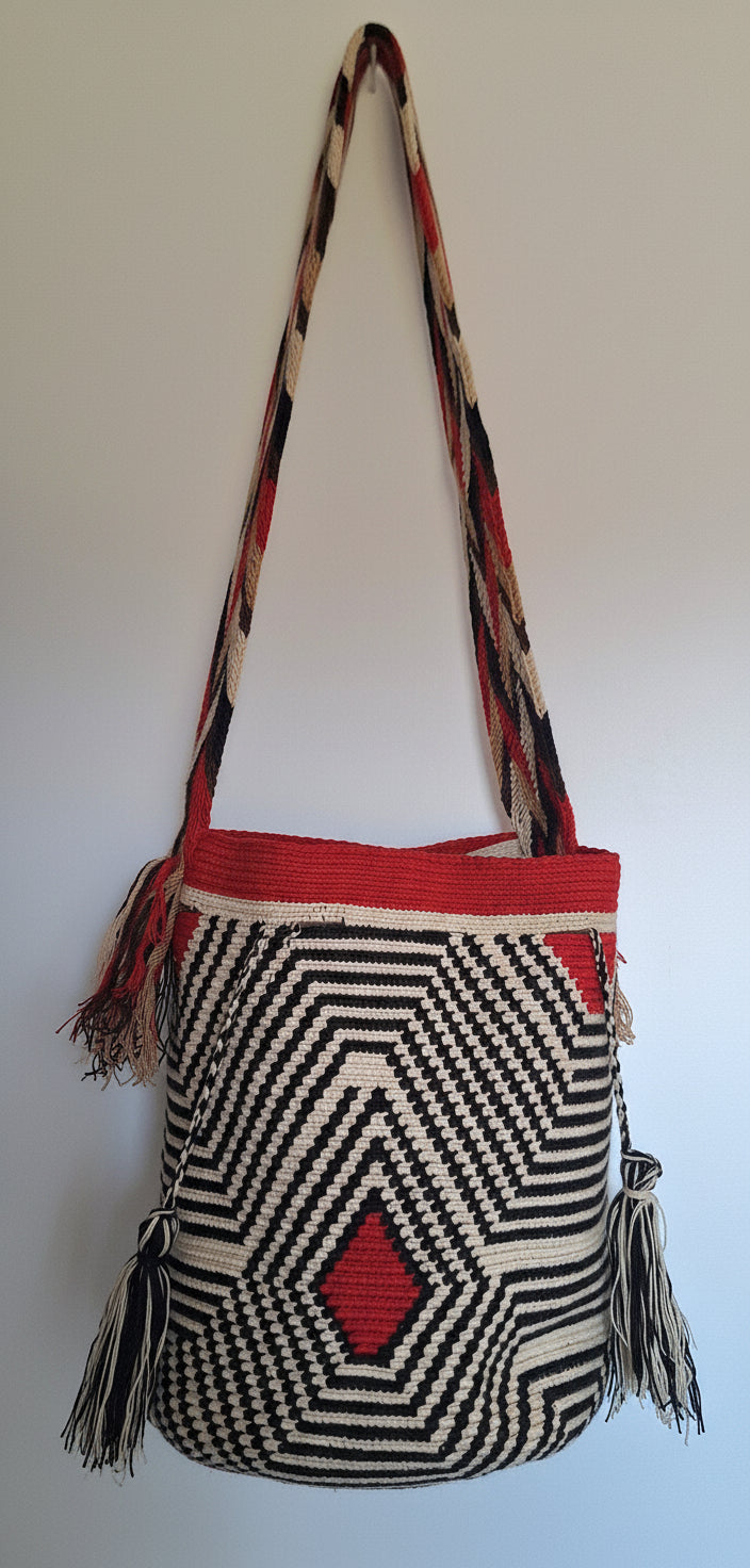 Detailed view of traditional Wayuu crochet technique in red and black with geometric design and tassels and crossbody strap fully extended. Large mochila bag is artisan-made and perfect for boho styling.