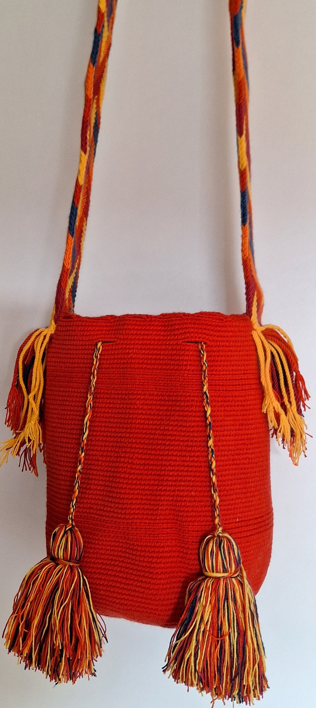 Detailed view of traditional Wayuu crochet technique and tassels on a red mochila bag with crossbody strap fully extended. Ethically and responsibly sourced.