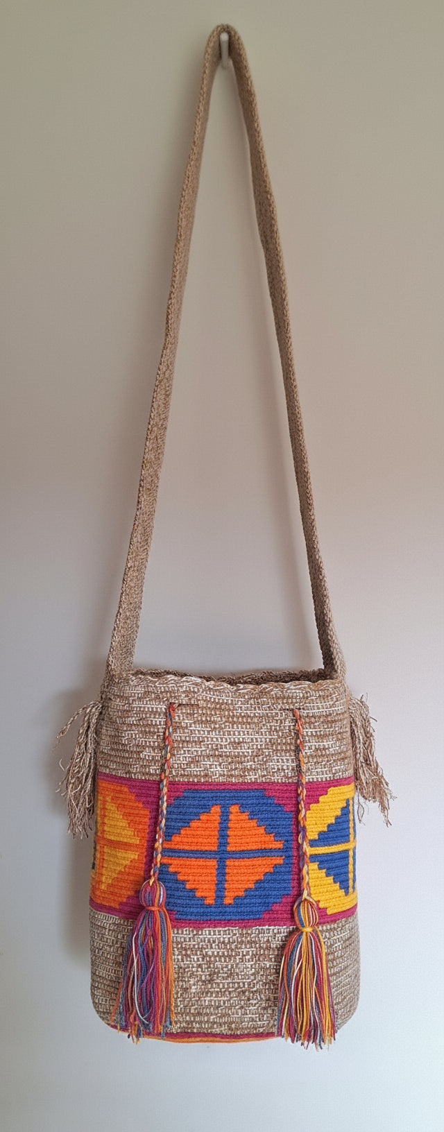 Detailed view of traditional Wayuu crochet technique with rhombus design in marbled beige, pink, blue, orange and yellow with crossbody strap fully extended. Mochila is responsibly hand-crafted; a boho festival essential.