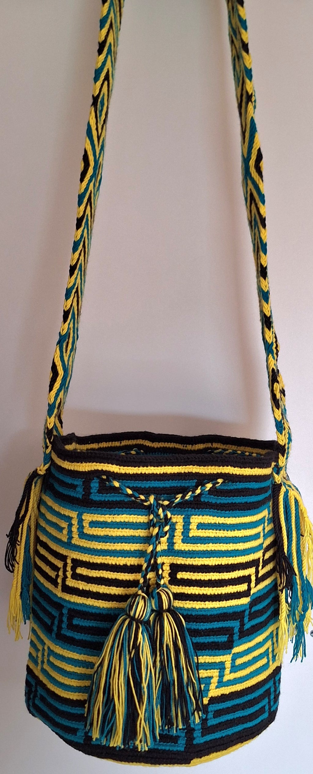 Detailed view of traditional Wayuu Mochila in yellow black and blue cotton threads with labyrinth design and crossbody strap fully extended. Hand-woven bag is hand-woven by artisans; great for boho-chic layers.