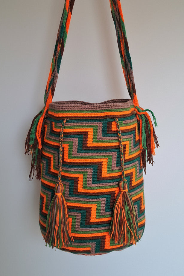 Detailed view of traditional Wayuu bag with zigzag design in orange, brown, grey and green and tassels and crossbody strap fully extended. Large Wayuu Bag is unique and traditionally crafted; adds a tribal touch to boho fits.