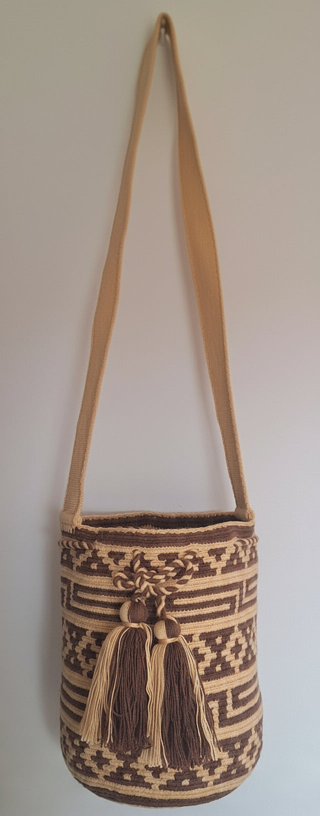 Detailed view of traditional medium-sized Wayuu Mochila with brown and beige geometric pattern, tassels and crossbody strap fully extended. Bag is authentic Wayuu heritage, ideal for eclectic outfits.