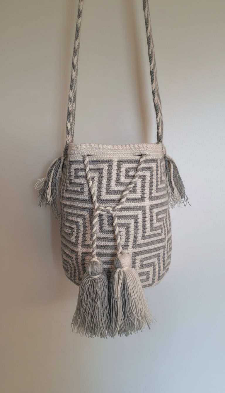 Detailed view of traditional medium-sized Wayuu Mochila in grey and white labyrinth pattern with tassels and crossbody strap fully extended. Bag supports indigenous weavers with every boho purchase.