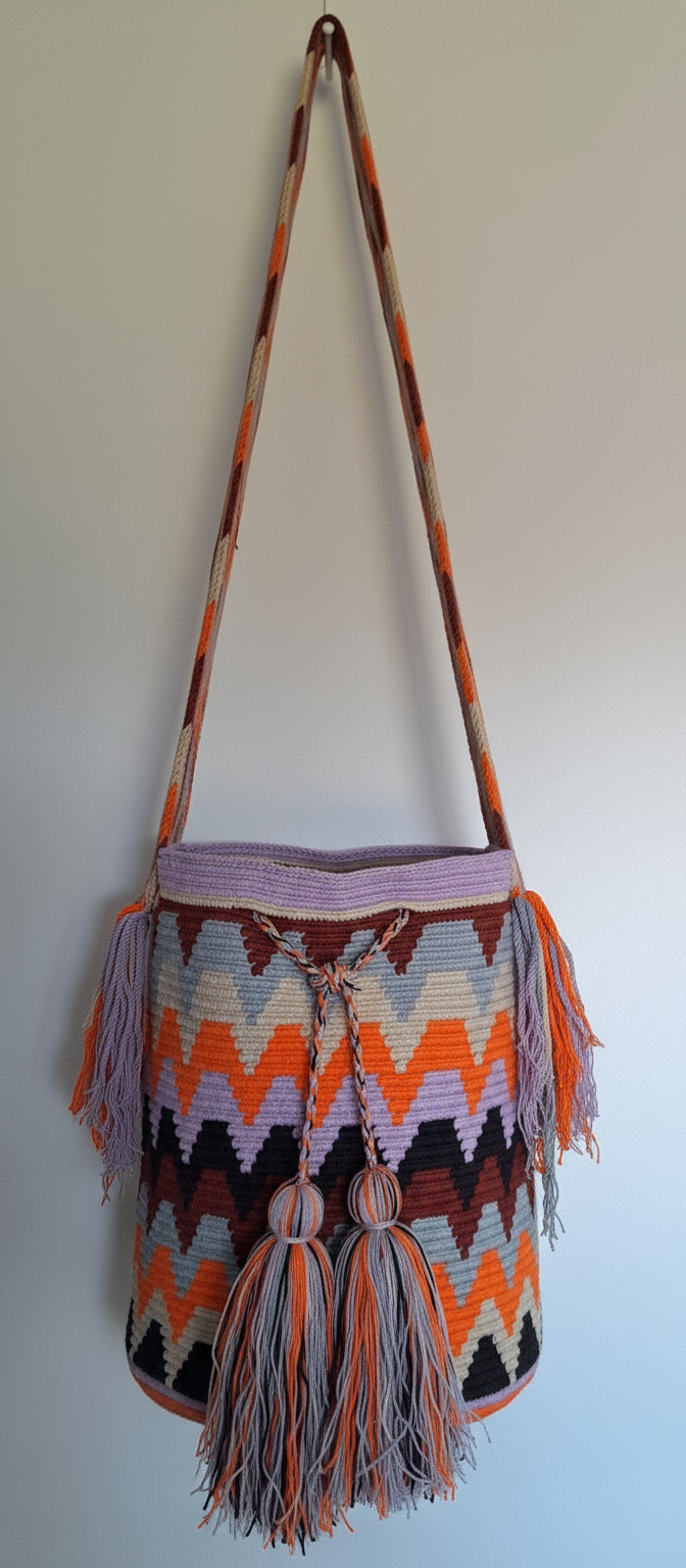Detailed view of traditional Wayuu crochet technique and tassels on a mochila bag in soft tones with crossbody strap fully extended. Ethically and responsibly sourced.