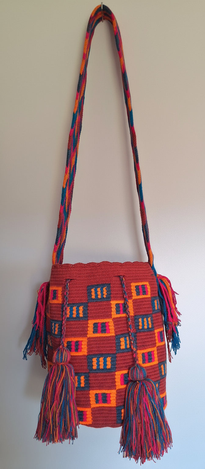 Detailed view of traditional Wayuu crochet technique and tassels on a red and orange mochila bag with crossbody strap fully extended. Ethically and responsibly sourced.