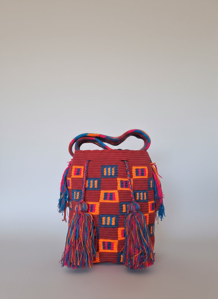 Detailed view of traditional Wayuu crochet technique and tassels on a mochila bag with design on red, orange and blues. Ethically and responsibly sourced.