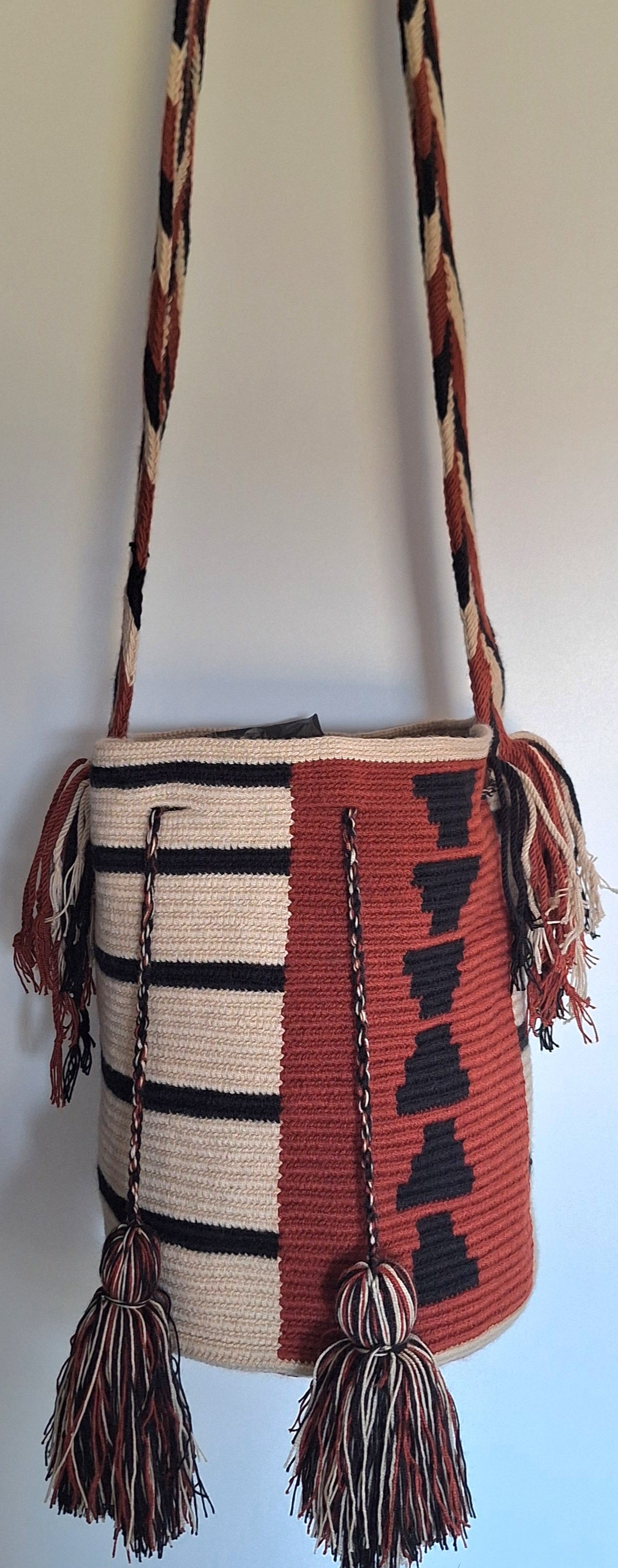 Detailed view of traditional Wayuu crochet technique and tassels on a mochila bag in red and beige with crossbody strap fully extended. Ethically and responsibly sourced.