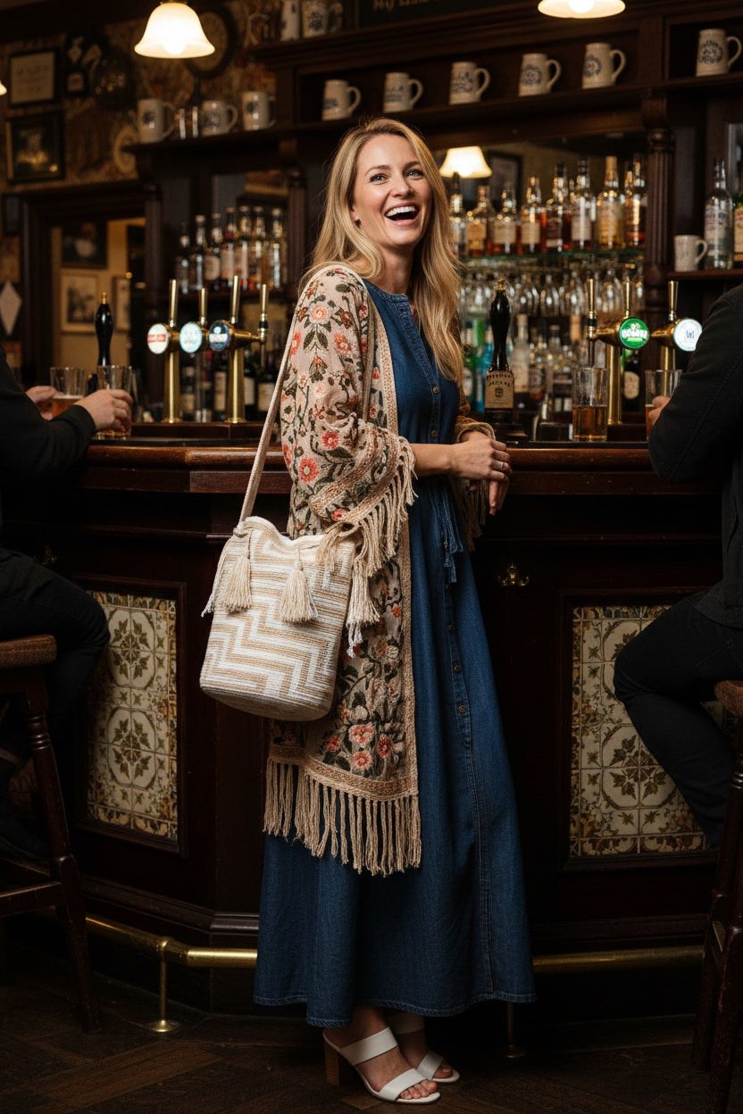 Woman wearing a handmade Wayuu shoulder bag with earthy hues in a bar, boho style. Ethically and responsibly sourced.