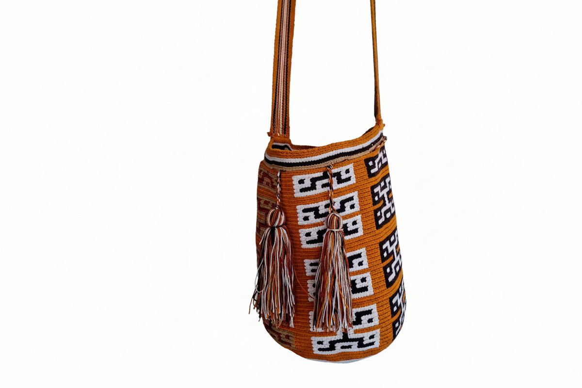 A handwoven Wayuu mochila shoulder bag in vibrant ochre, black, and white, hanging on a studio wall. Traditional patterns and ethical sourcing, makes bag a perfect gift