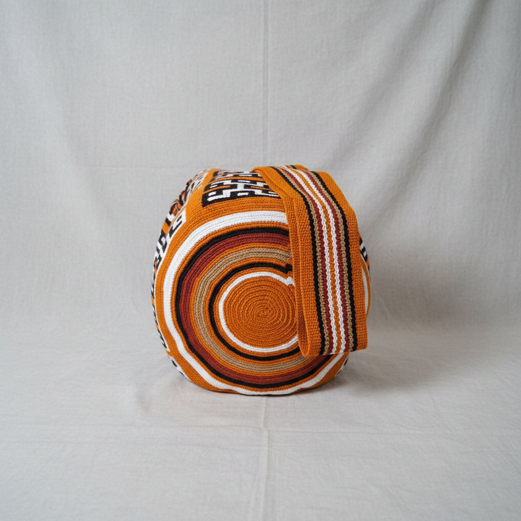A handwoven wayuu bucket bag or wide strap, featuring concentric rings of ochre, brown, red beige, black, and white, and geometric patterns, with focus on authentic base of bag and crossbody strap design.
