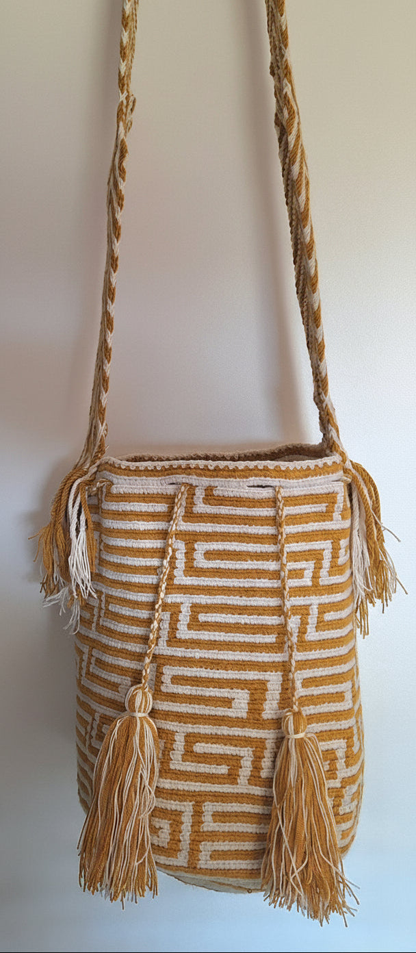 Detailed view of traditional Wayuu crochet technique and tassels on a mochila bag in gold and white with crossbody strap fully extended. Ethically and responsibly sourced.