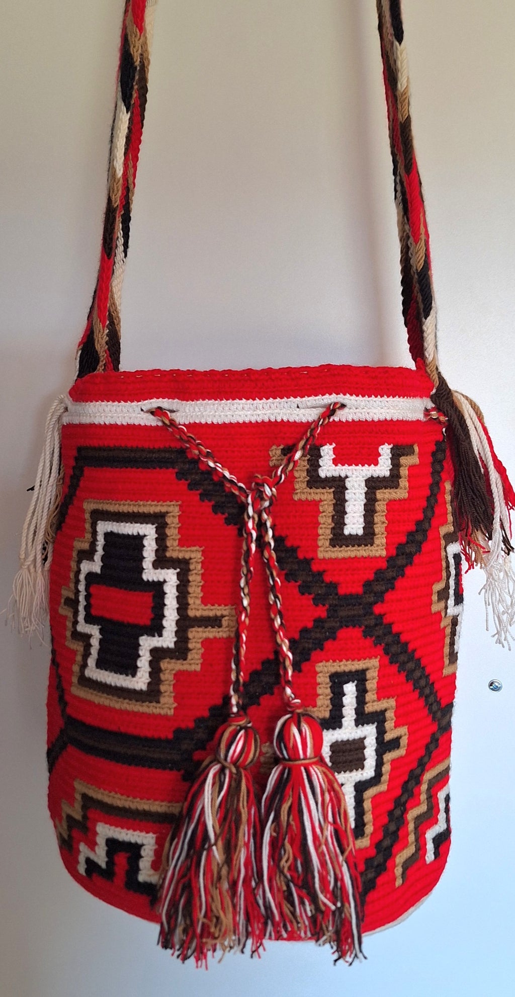 Detailed view of traditional Wayuu crochet technique and tassels on a red and white mochila bag with crossbody strap fully extended. Ethically and responsibly sourced.