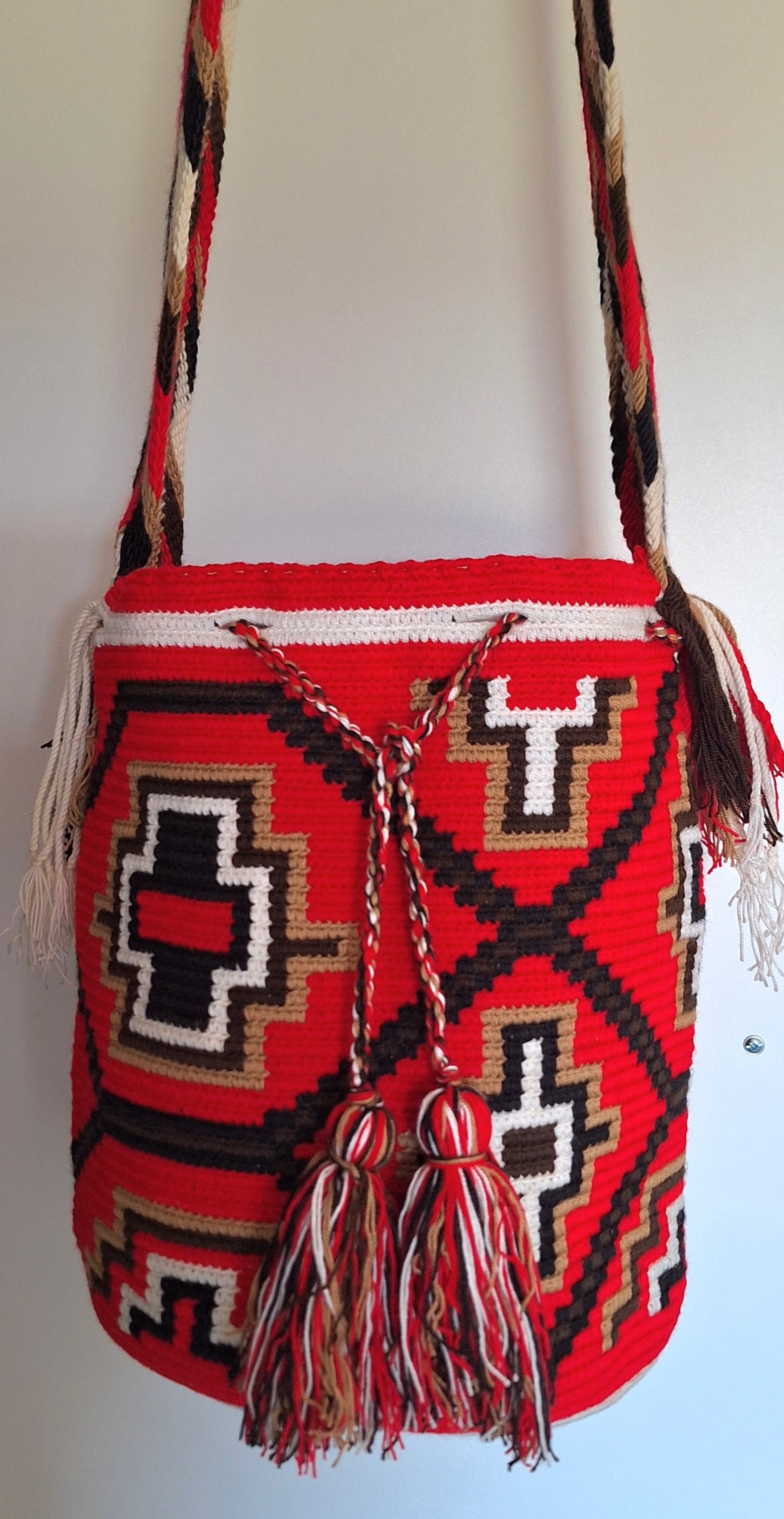 Detailed view of traditional Wayuu crochet technique and tassels on a red and white mochila bag with crossbody strap fully extended. Ethically and responsibly sourced.