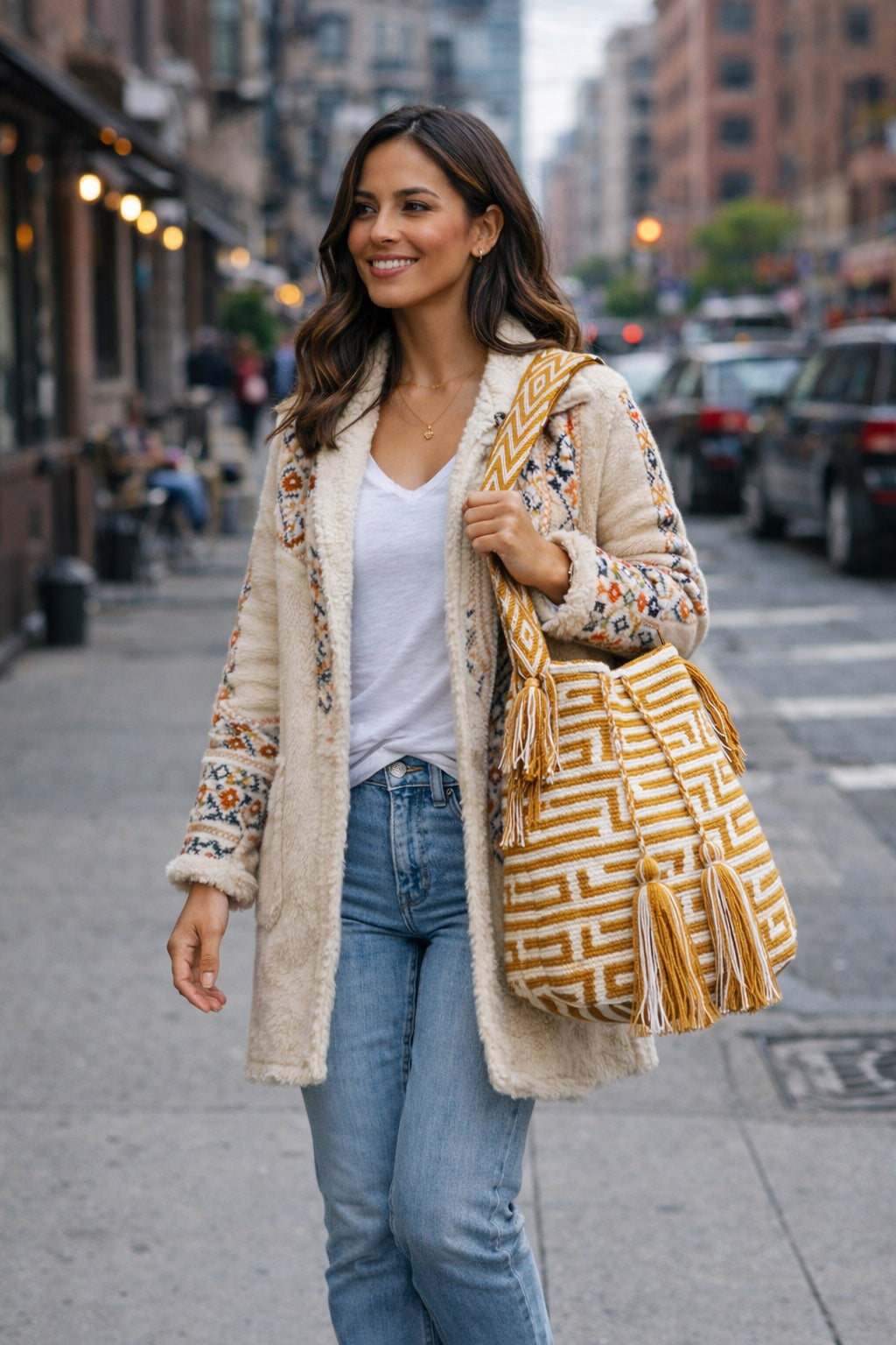 Woman wearing a gold and white handmade Wayuu shoulder bag walking along street, boho style. Ethically and responsibly sourced.